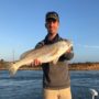 andrew juran-holding-redfish-on-boat-near-sunset-wearing-fishing-clothes