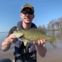 andrew juran holding pale smallmouth bass on boat in dirty water