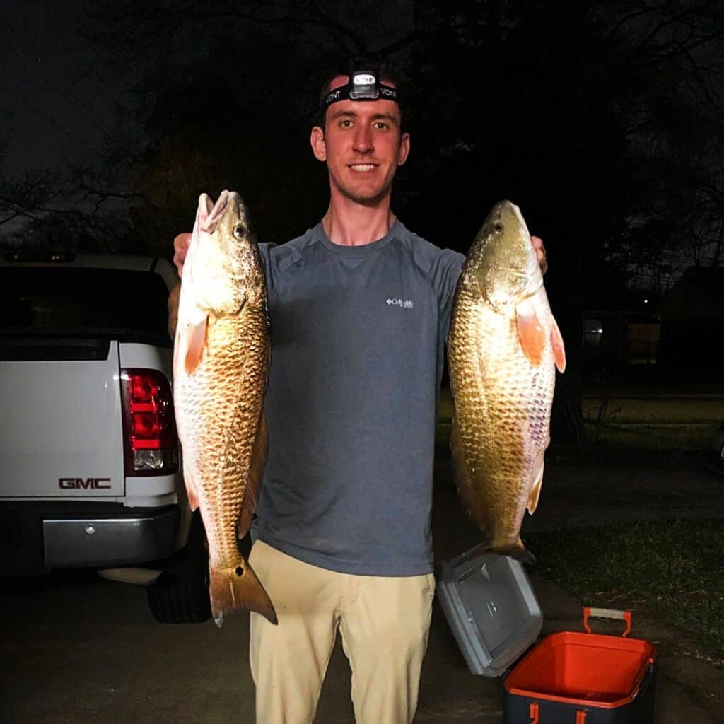 andrew juran holding two redfish at night wearing head lamp